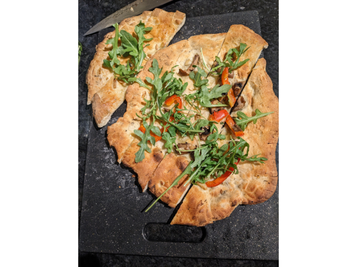 Flatbread on a cutting board with arugula, garlic and peppers.